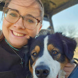 Person with glasses holding a dog inside a vehicle