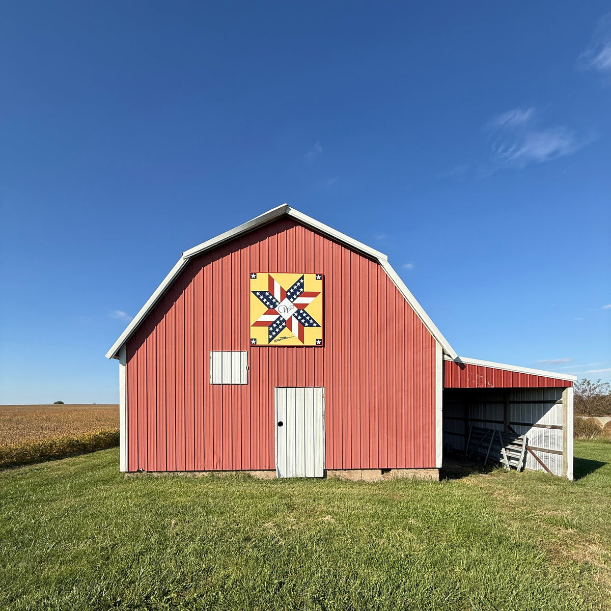 Red barn with a quilt pattern on its side against a clear blue sky.